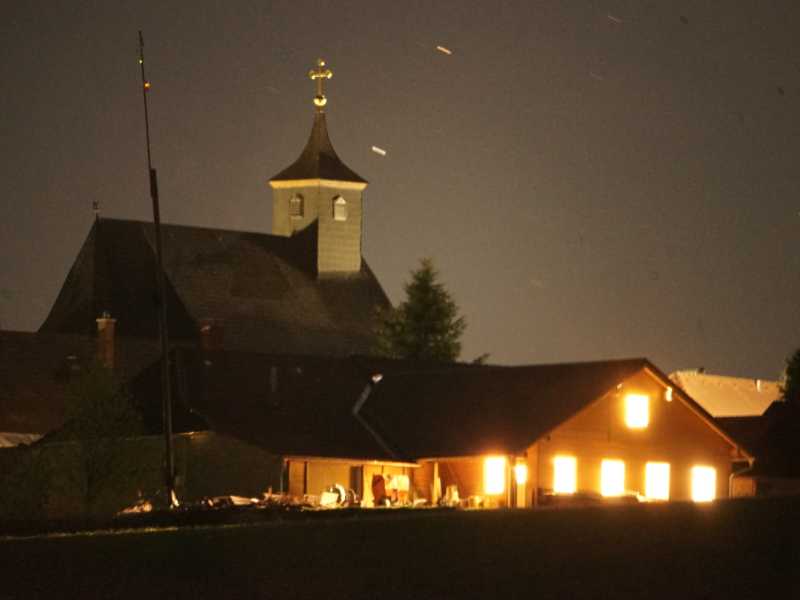 Veranstaltungszentrum mit erleuchteten Fenstern, dahinter die Kirche unterm Nachthimmel